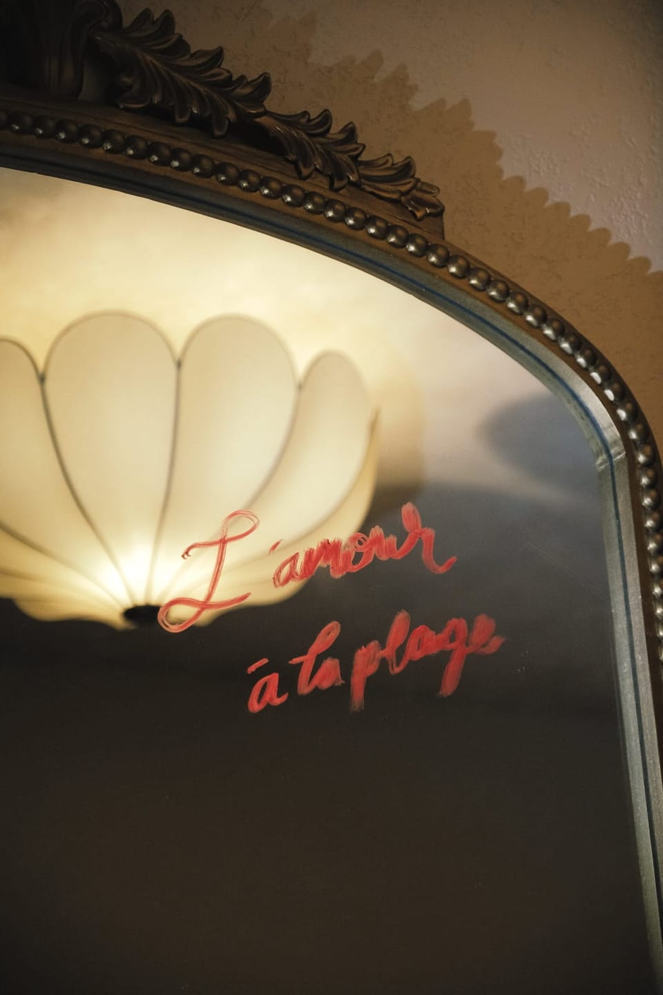 L'amour à la plage written in red on a mirror, a lamp reflected behind